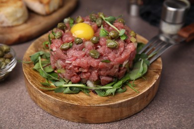 Photo of Tasty beef steak tartare served with yolk, capers and microgreens on brown table, closeup