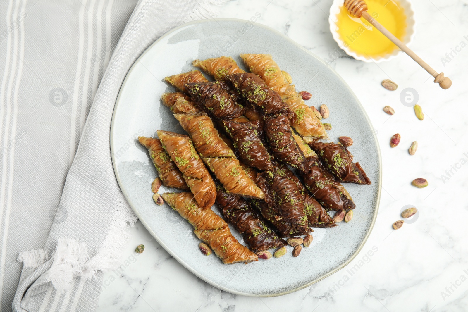 Photo of Delicious baklava with pistachio nuts and honey on white marble table, flat lay