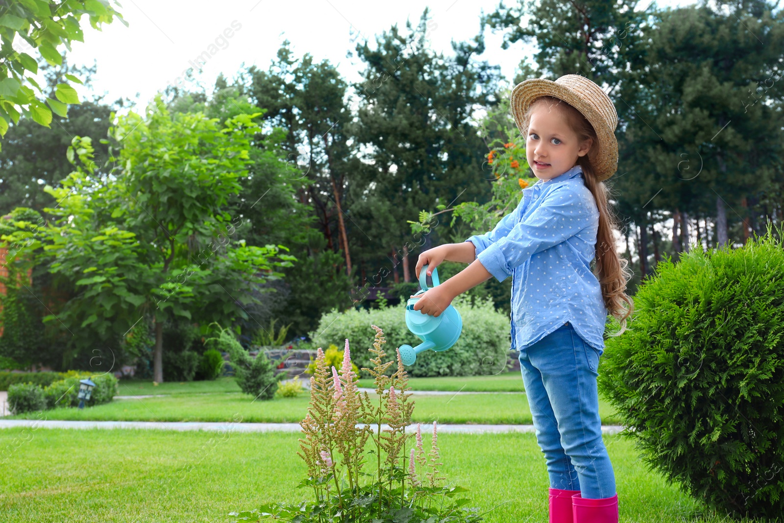 Photo of Little girl watering flowers in backyard. Home gardening