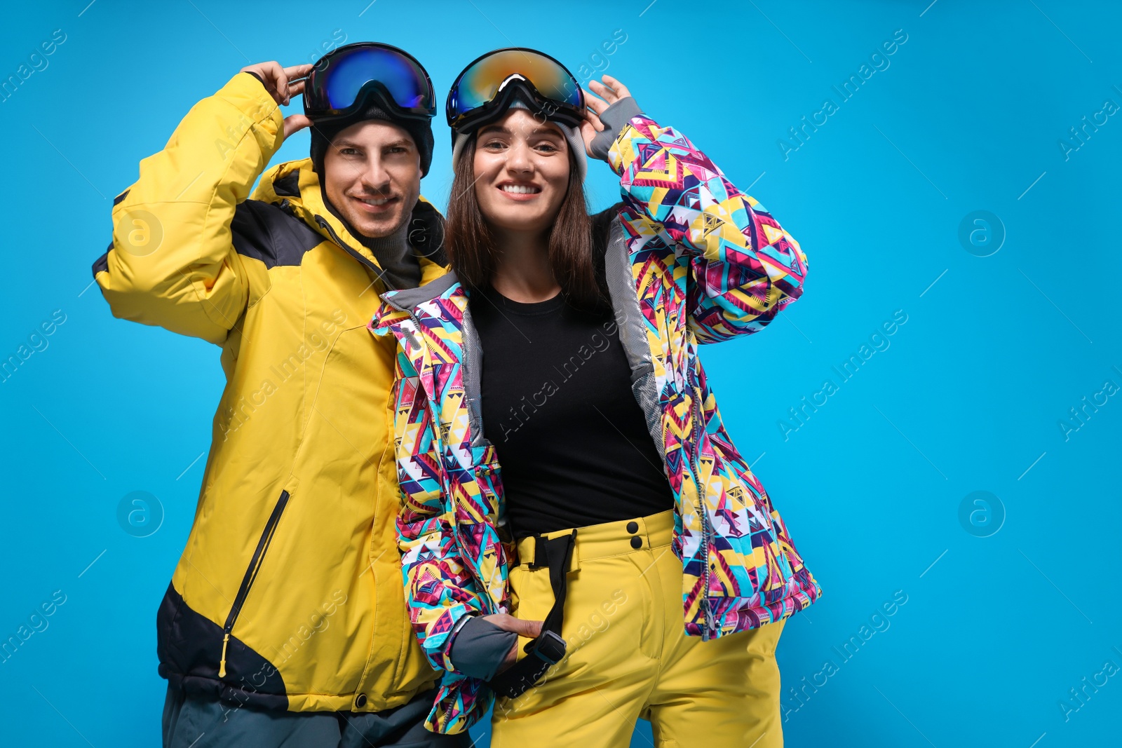 Photo of Couple wearing stylish winter sport clothes on light blue background, low angle view