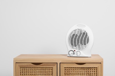 Photo of Electric fan heater on wooden cabinet indoors. Space for text
