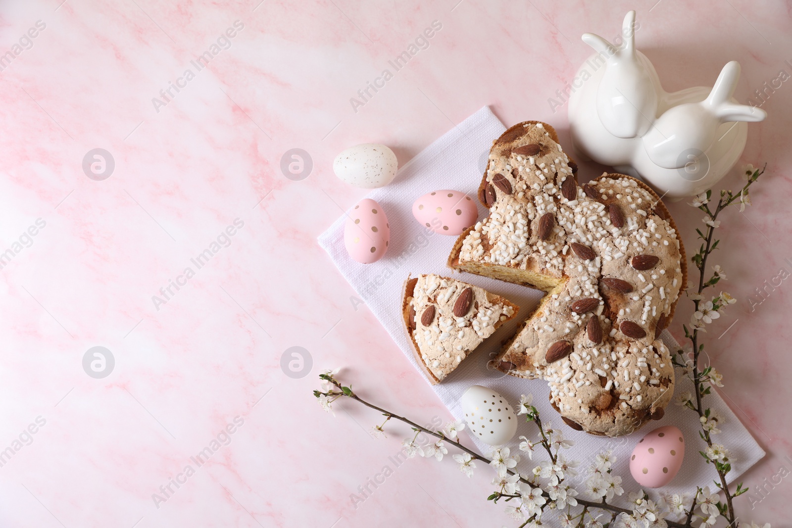 Photo of Delicious Italian Easter dove cake (traditional Colomba di Pasqua), painted eggs, figure of rabbits and branch with flowers on pink marble table, flat lay. Space for text