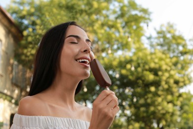 Photo of Beautiful young woman eating ice cream glazed in chocolate on city street, space for text