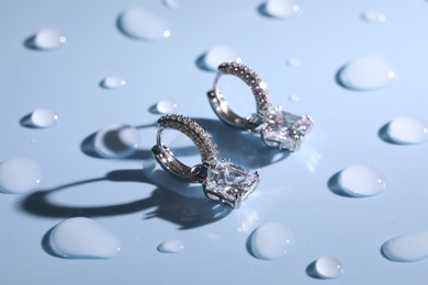 Elegant earrings on light blue surface covered with water drops. Luxury jewelry