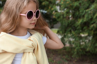 Photo of Girl in stylish sunglasses near spruce trees outdoors. Space for text