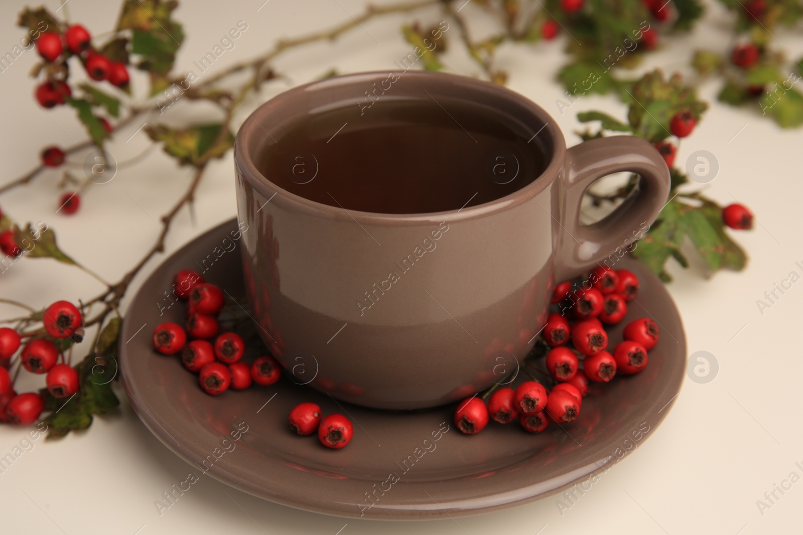 Photo of Aromatic hawthorn tea in cup and berries on beige table, closeup