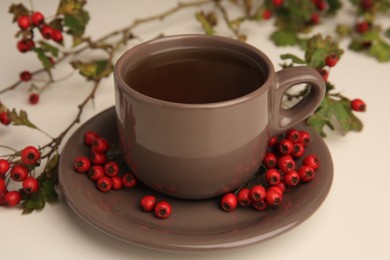 Photo of Aromatic hawthorn tea in cup and berries on beige table, closeup