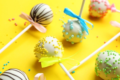 Different tasty cake pops with sprinkles on yellow background