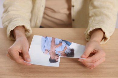 Woman holding torn photo at wooden table, closeup. Divorce concept