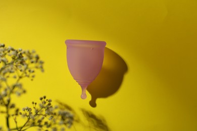 Photo of Menstrual cup and flowers on yellow background, flat lay. Space for text