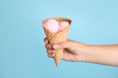 Woman holding delicious ice cream in wafer cone on blue background, closeup