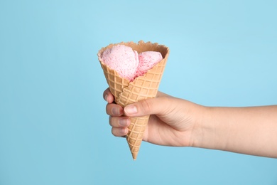 Photo of Woman holding delicious ice cream in wafer cone on blue background, closeup