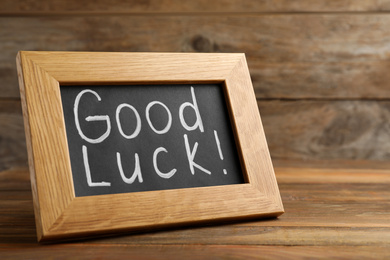 Photo of Blackboard with phrase GOOD LUCK on wooden table