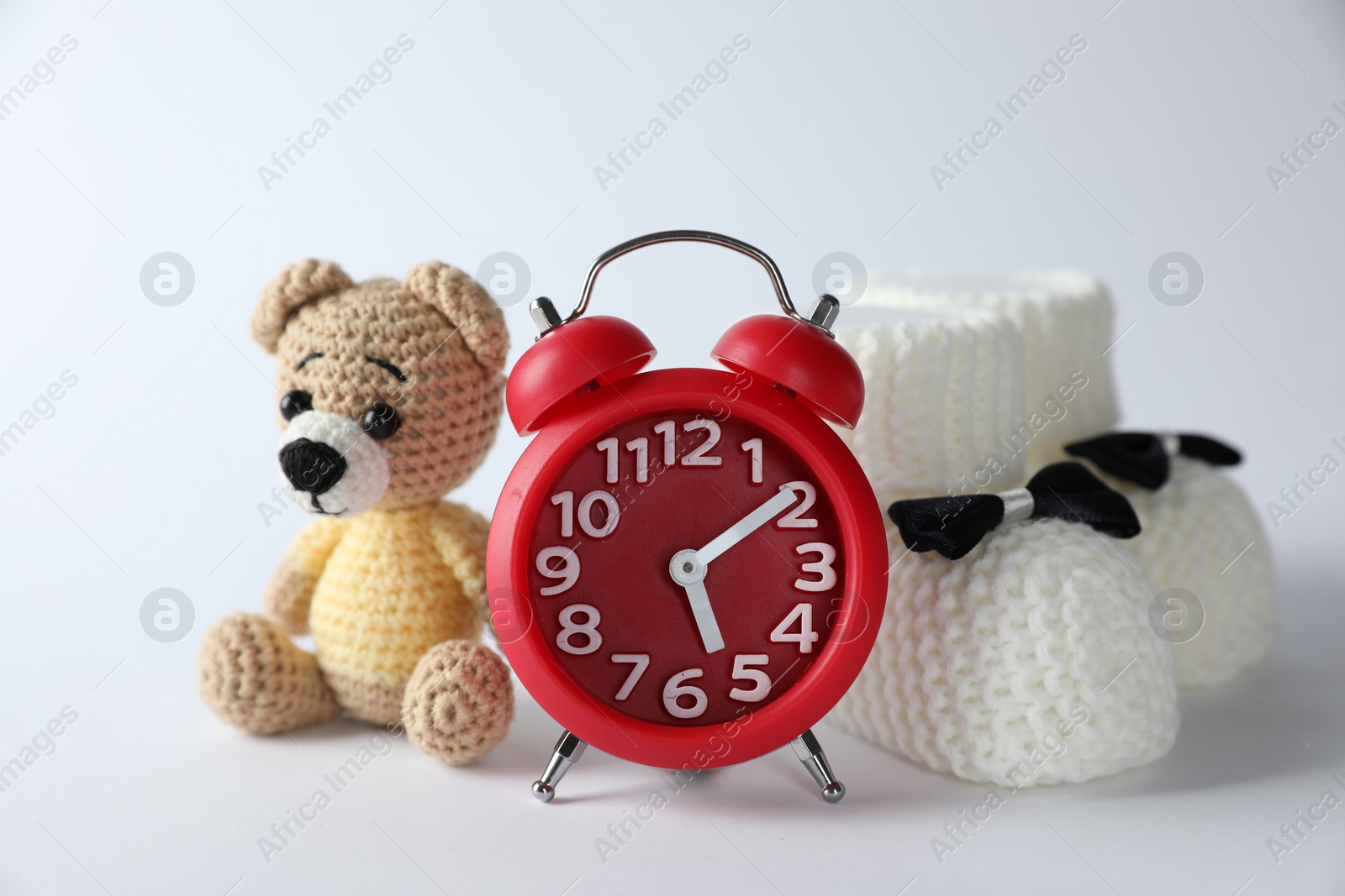 Photo of Alarm clock, toy bear and baby booties on white background. Time to give birth