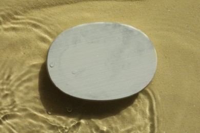 Photo of Stylish presentation for product. Stone podium in water on sand, top view