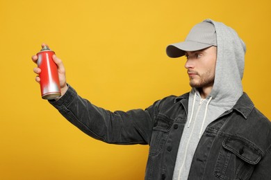 Handsome man holding can of spray paint on yellow background