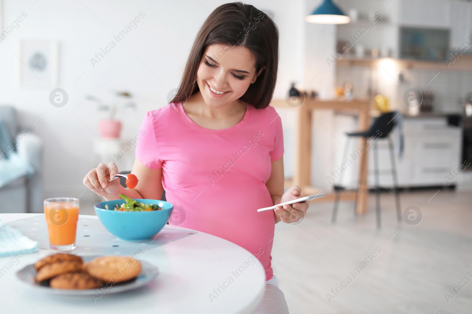 Photo of Young pregnant woman eating vegetable salad at table in kitchen