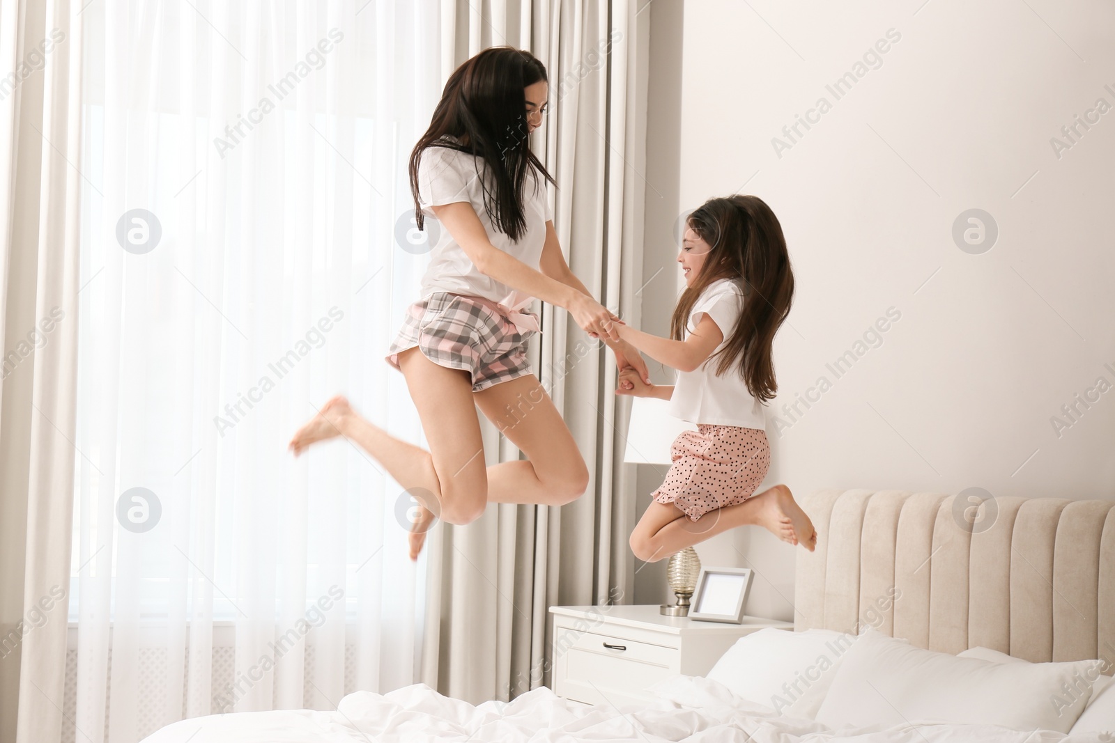 Photo of Young mother and her daughter jumping on bed at home