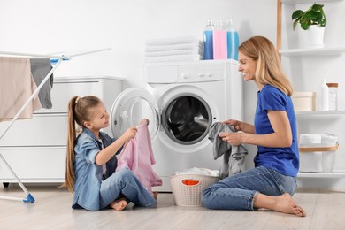 Photo of Mother and daughter taking out dirty clothes from basket in bathroom