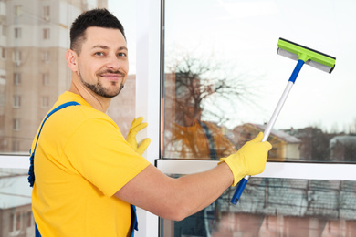 Photo of Professional janitor cleaning window with squeegee indoors