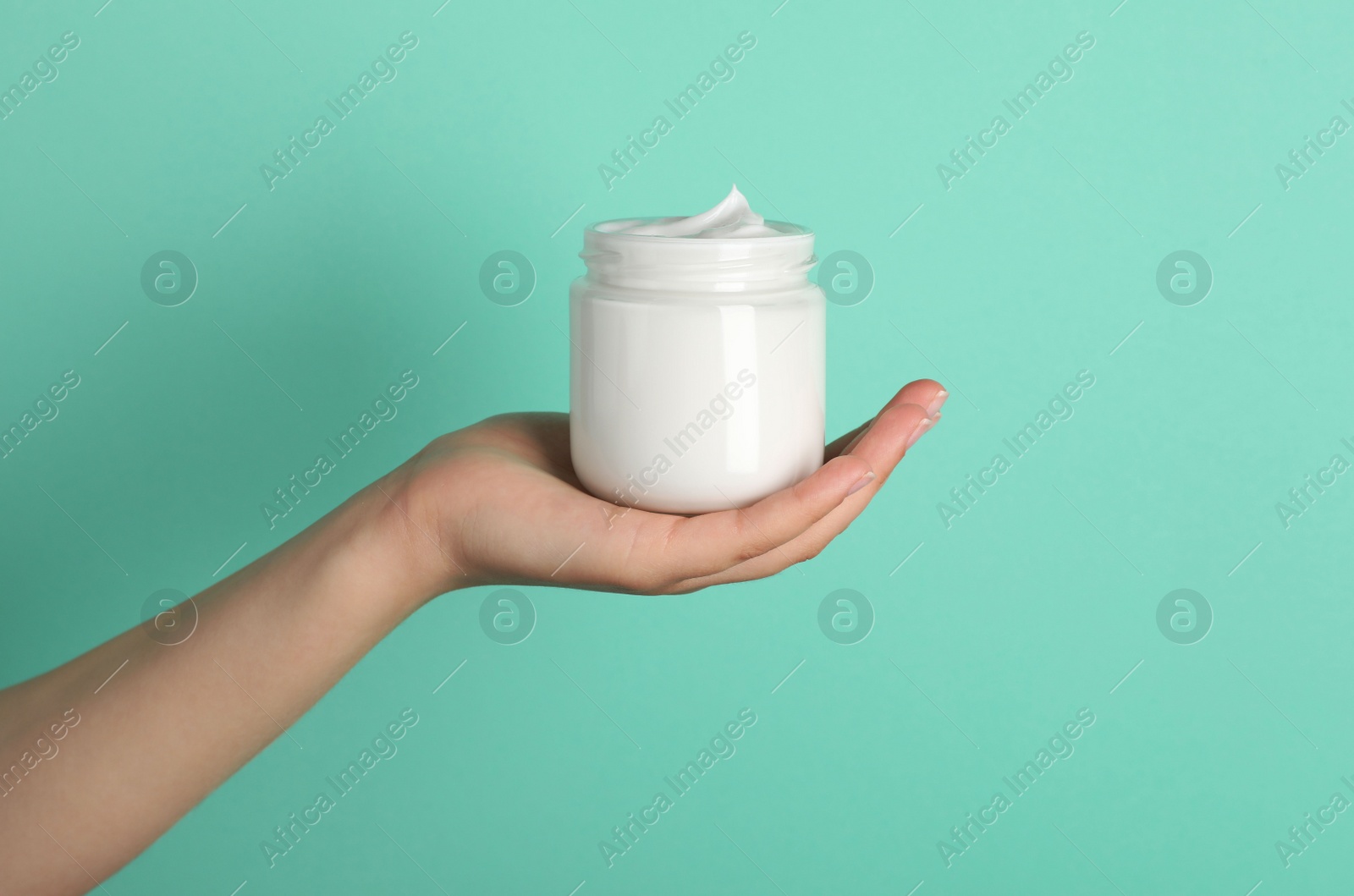 Photo of Woman holding jar of face cream on light turquoise background, closeup