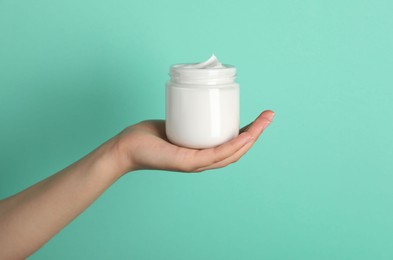 Photo of Woman holding jar of face cream on light turquoise background, closeup
