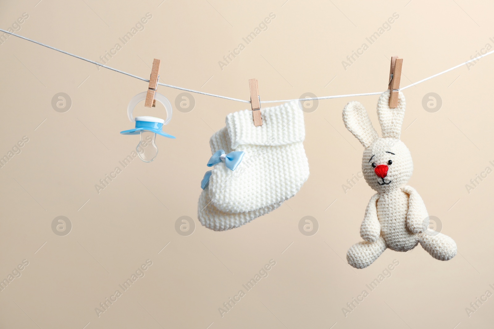 Photo of Knitted booties, pacifier and toy bunny hanging on washing line against color background. Baby accessories