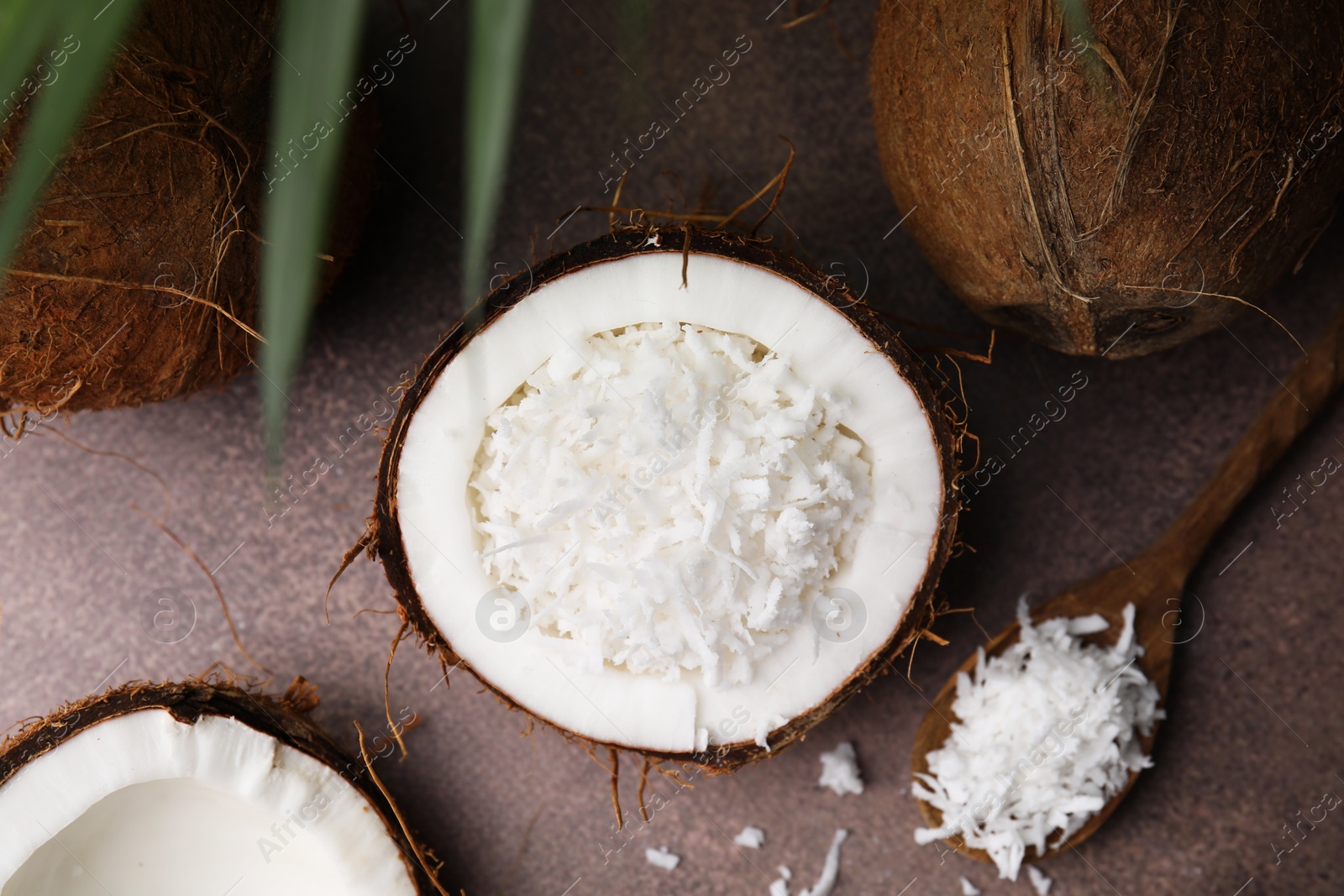 Photo of Coconut flakes in nut shell and spoon on brown table, flat lay