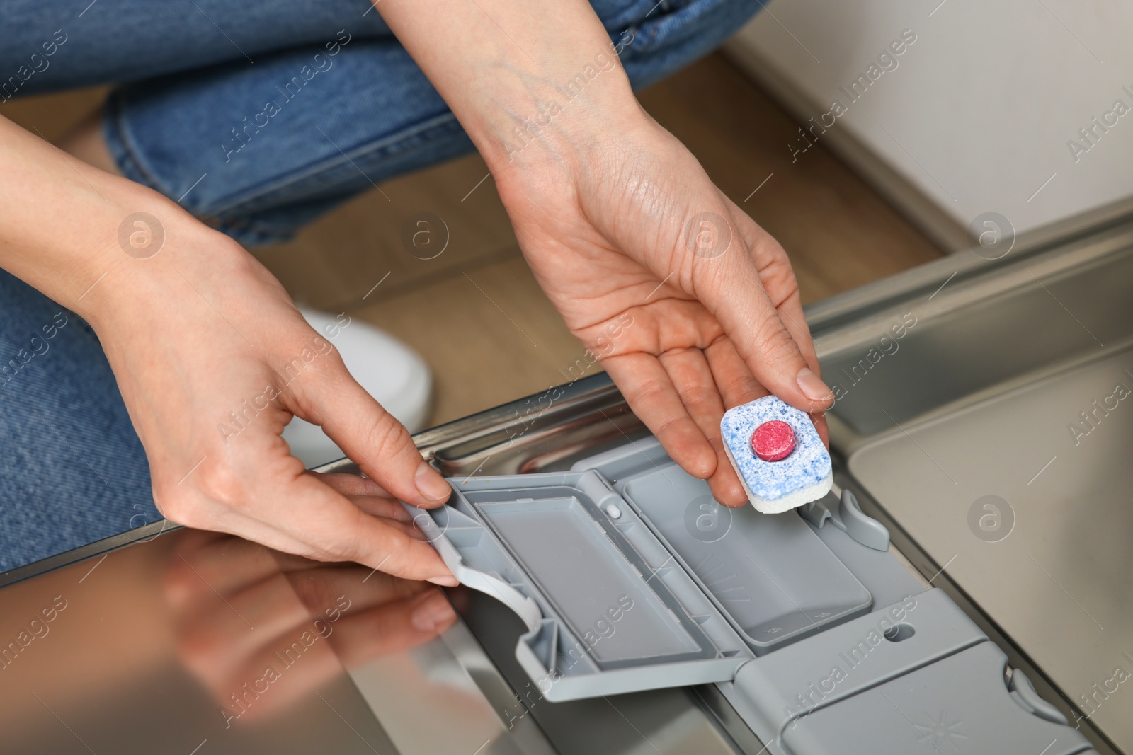 Photo of Woman putting detergent tablet into open dishwasher, closeup