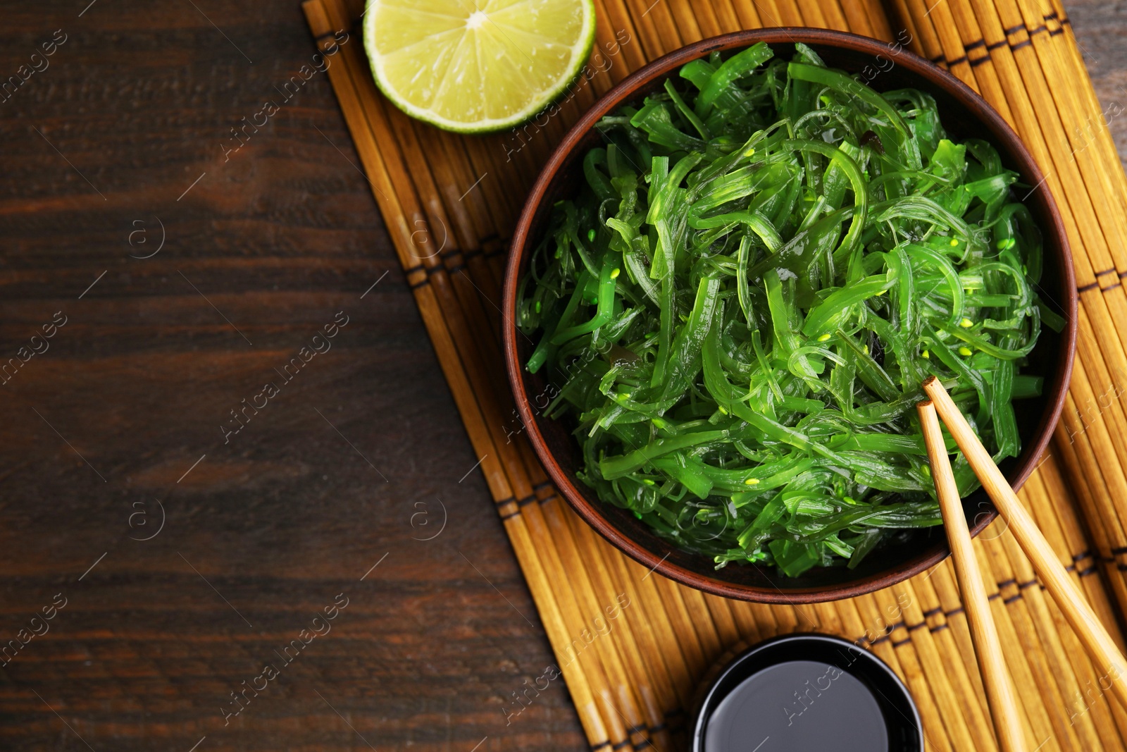 Photo of Tasty seaweed salad in bowl served on wooden table, flat lay. Space for text