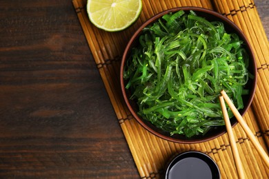 Photo of Tasty seaweed salad in bowl served on wooden table, flat lay. Space for text