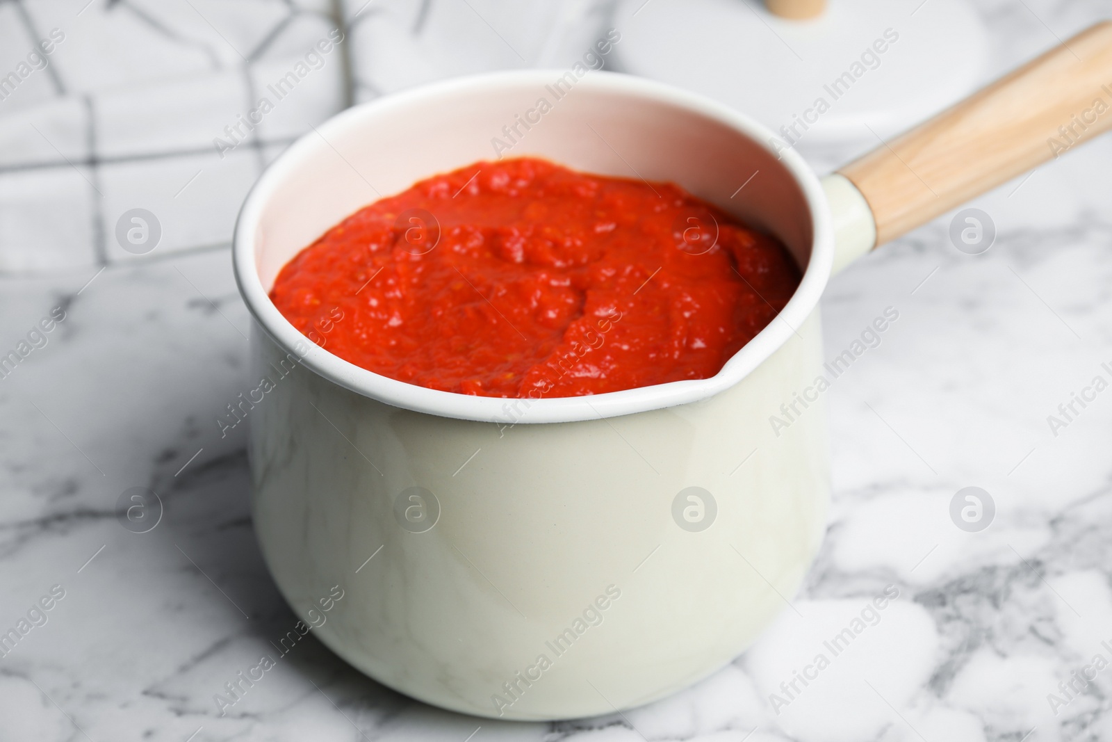 Photo of Delicious tomato sauce in pan on marble table