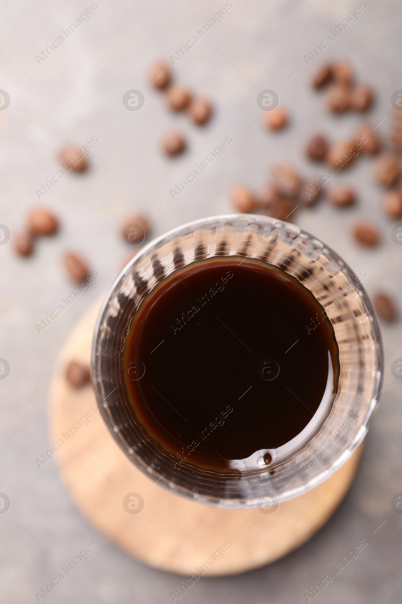 Photo of Shot glass with coffee liqueur and beans on light grey table, top view