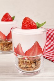 Photo of Glassestasty yogurt with muesli and strawberries served on white wooden table