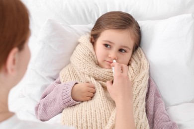 Mother using nasal spray to treat her little daughter on bed, above view