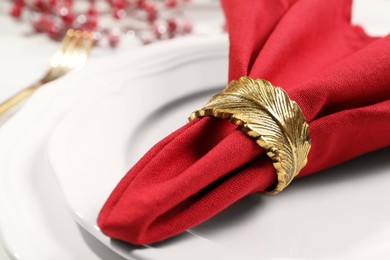 Photo of Red fabric napkin with beautiful decorative ring on white table, closeup