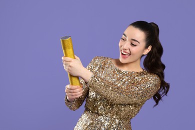 Photo of Young woman blowing up party popper on purple background, space for text
