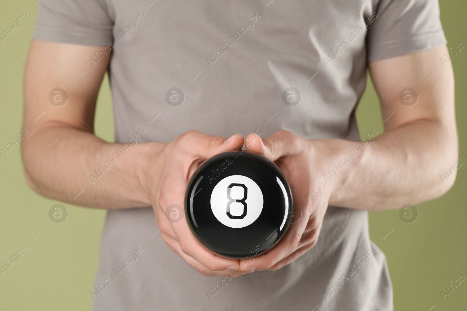 Photo of Man holding magic eight ball on olive background, closeup