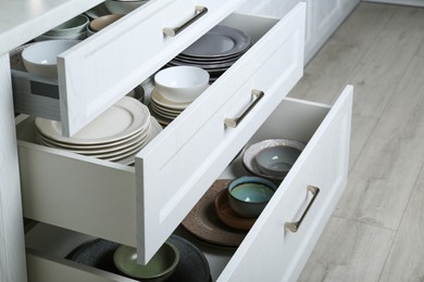 Photo of Open drawers with different plates and bowls in kitchen