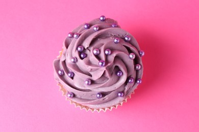 Photo of Delicious cupcake with bright cream and sprinkles on pink background, top view