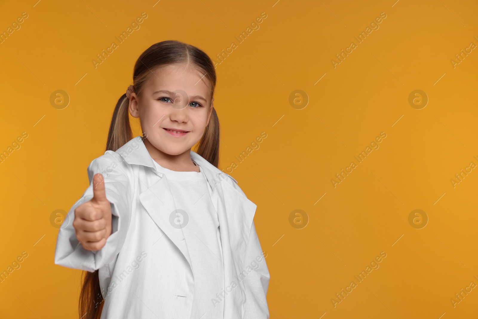 Photo of Little girl in medical uniform showing thumb up on yellow background. Space for text