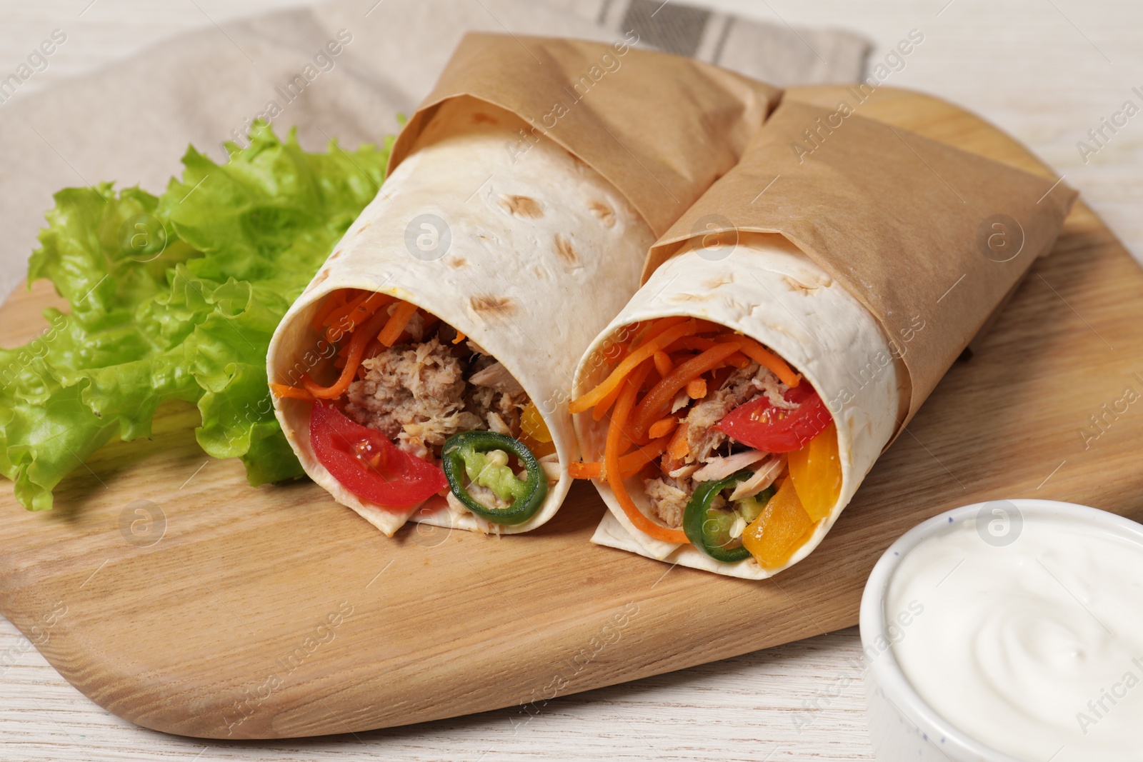 Photo of Delicious tortilla wraps with tuna on white wooden table
