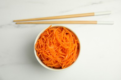 Photo of Delicious Korean carrot salad and chopsticks on white marble table, flat lay