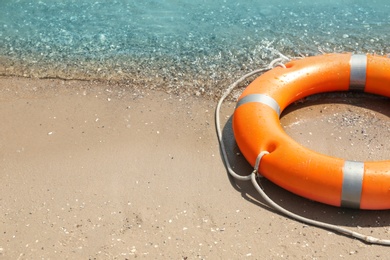 Photo of Orange life buoy on sand near sea, closeup. Emergency rescue equipment