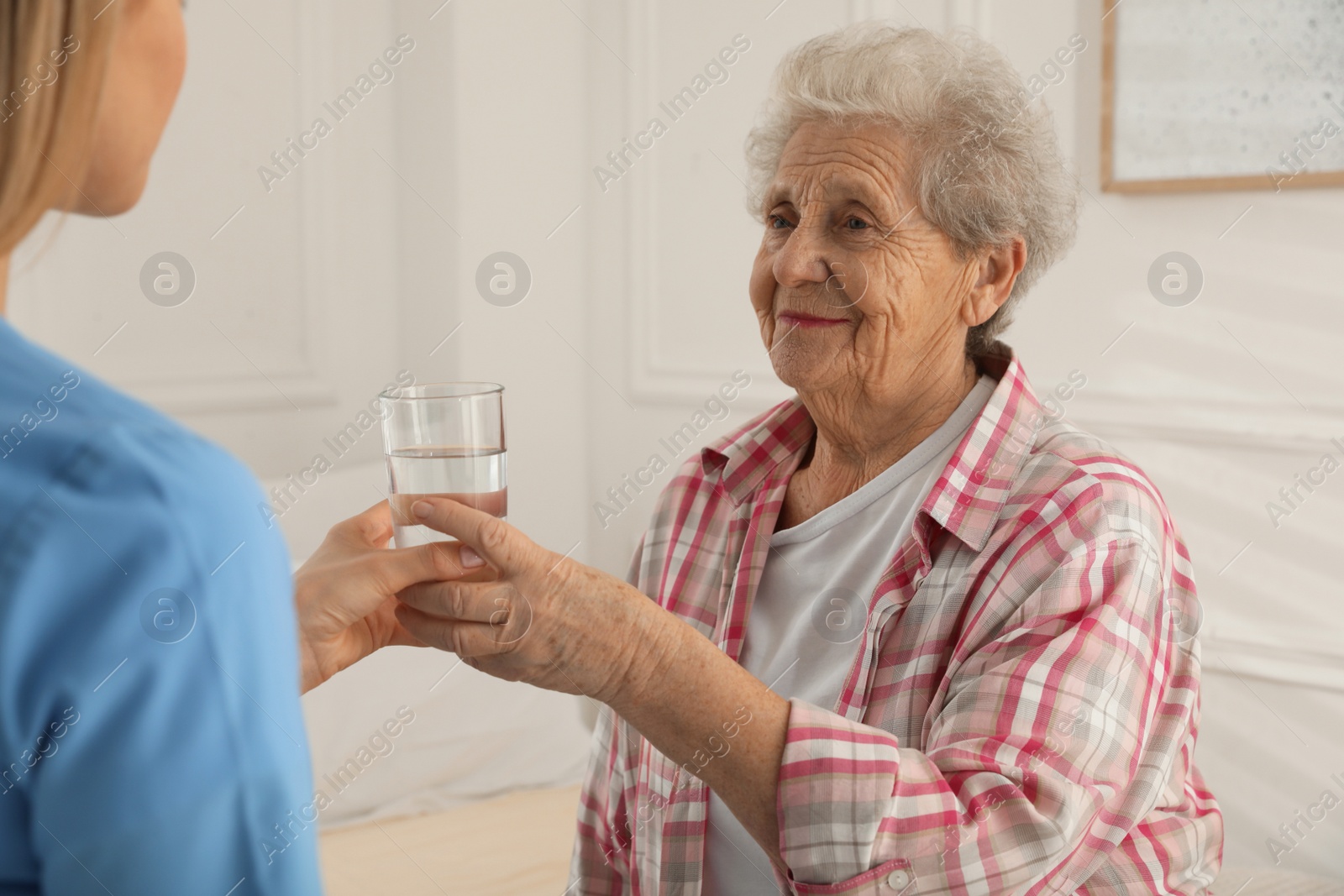 Photo of Young caregiver giving water to senior woman in room. Home care service