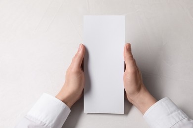 Photo of Woman holding blank card at white table, top view. Mockup for design