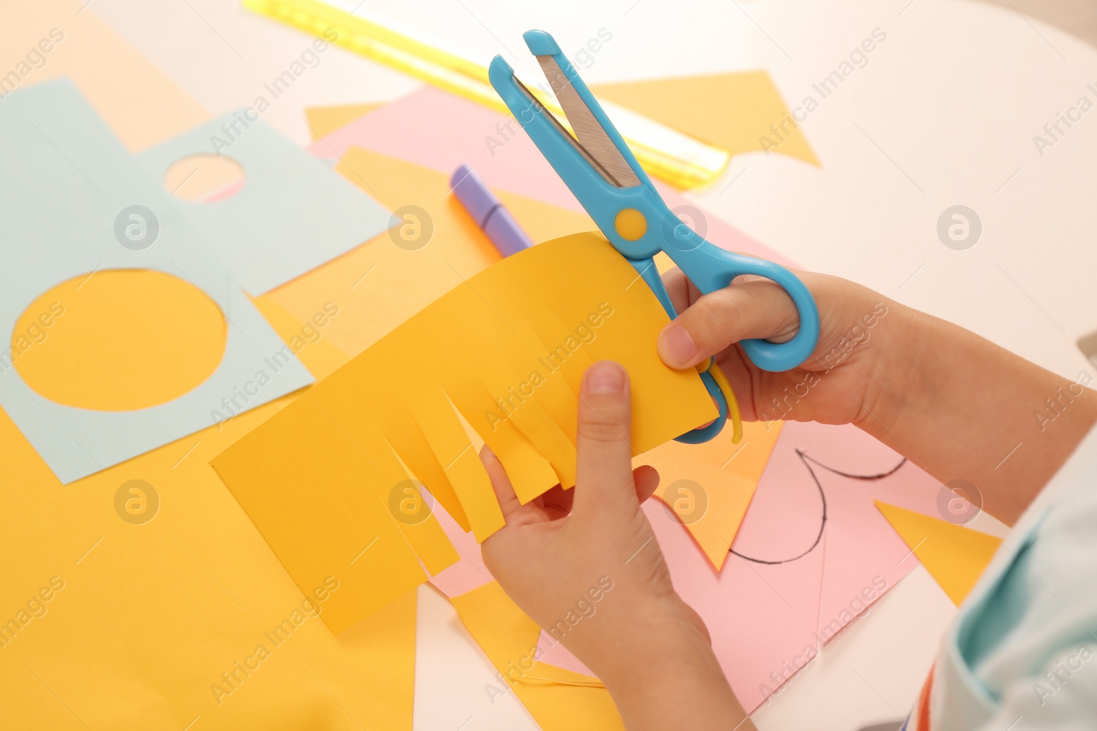 Photo of Little boy cutting color paper with scissors at table indoors, closeup