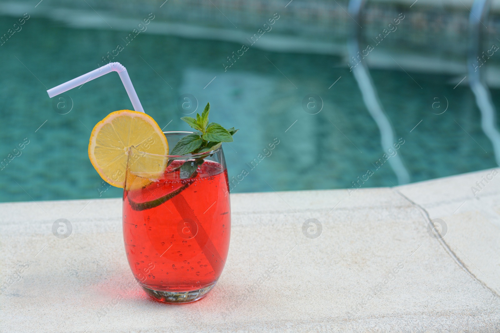 Photo of Glass of delicious cocktail near swimming pool, space for text. Refreshing drink