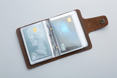 Woman holding leather card holder with credit cards on light grey background, top view