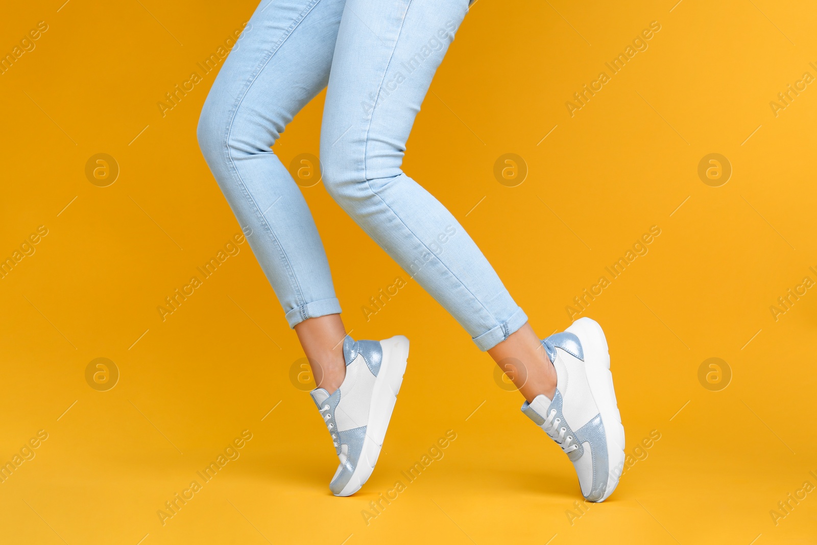 Photo of Woman wearing stylish sneakers on yellow background, closeup